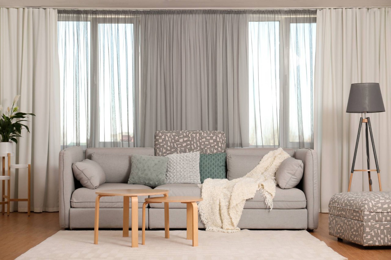 Cozy, chic living room interior with custom drapery on large windows behind the neutral couch at Dreamweaver Interiors & Fabrics near Rehoboth Beach, DE